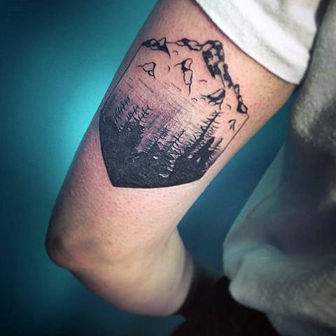 Abstract geometric forest and mountain black ink bicep tattoo on man