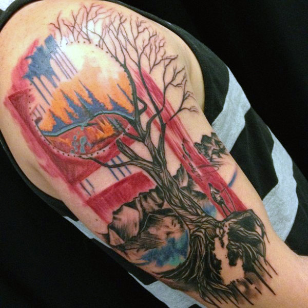Man with upper arm tattoo of man standing next to surreal tree of life