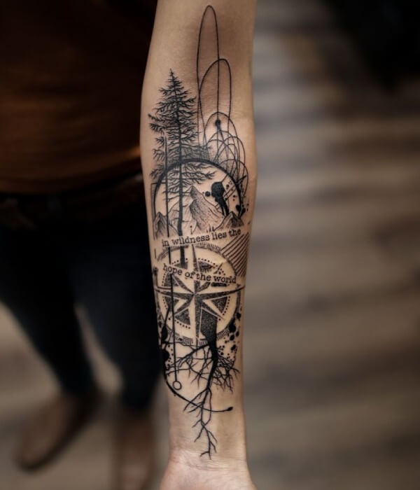 Abstract forest tattoo on a forearm combining fine-line pine trees, mountains, geometric shapes, compass elements, and roots in black ink, creating a symbolic nature-inspired design on real human skin.