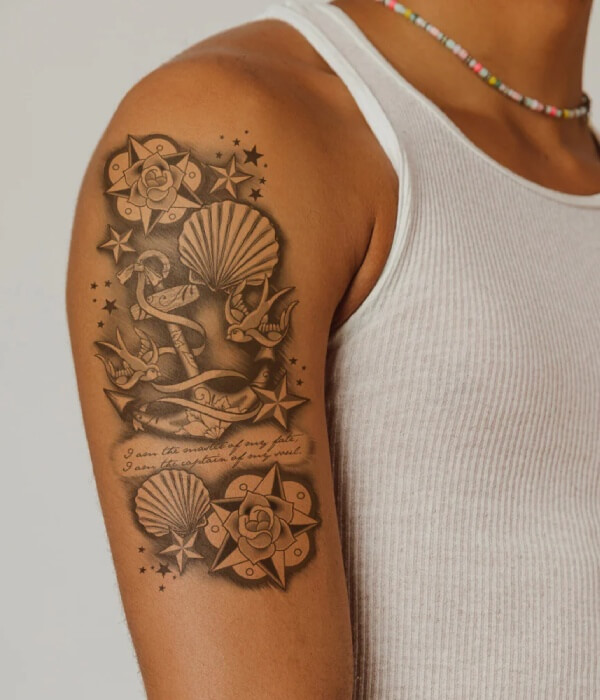 Detailed anchor and seashell tattoo on the upper arm featuring nautical elements, stars, roses, and birds in a vintage black and grey tattoo style.
