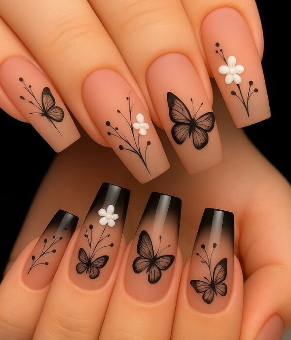 Close-up of nude coffin-shaped nails featuring elegant butterfly nail tattoos with black line art, delicate floral accents, and a soft gradient French tip design.