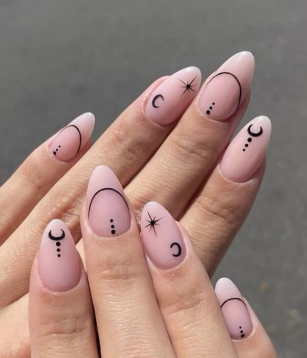 Close-up of soft pink almond-shaped nails featuring minimalist celestial nail tattoos, including crescent moons, stars, dots, and fine black line accents.