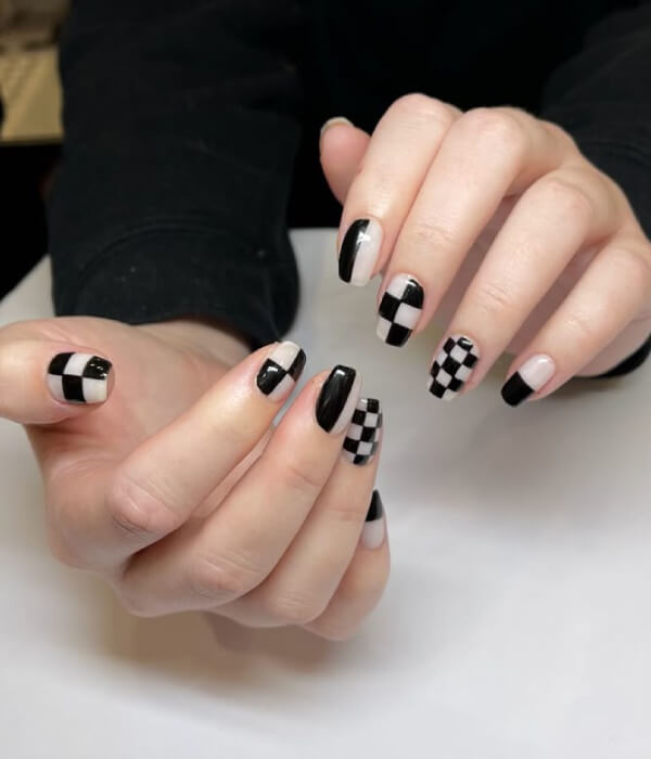 Close-up of hands with black-and-white checkered pattern nail tattoos, featuring glossy squares and minimalist geometric nail art on short nails.