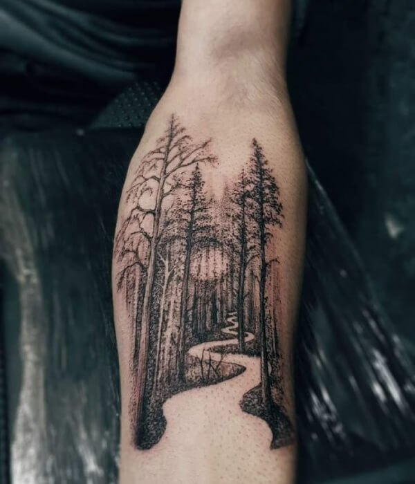 Detailed forest pathway tattoo on a forearm, featuring tall trees lining a winding path in black and grey fine-line style, creating a serene and symbolic nature-inspired tattoo on real human skin.
