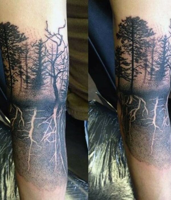 Forest roots tattoo on a forearm, showing tall trees above ground with detailed roots below the surface, shaded in black and grey to symbolize strength, growth, and deep connection to nature on real human skin.