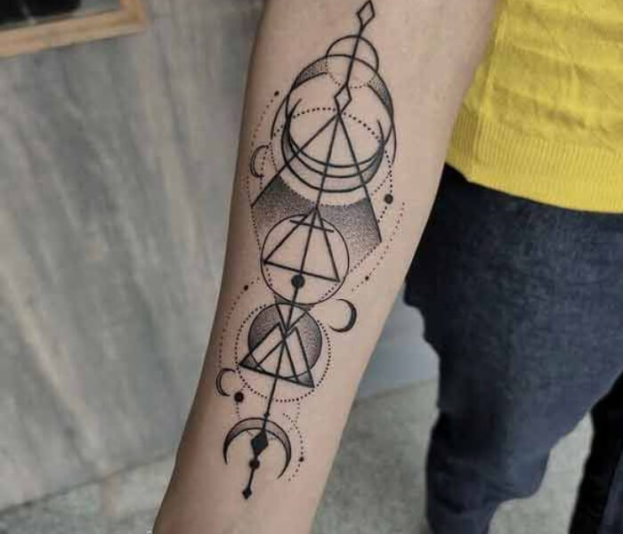 Geometric Zodiac Tattoo 1 - Trending Tattoo Geometric zodiac tattoo featuring fine-line circles, triangles, and celestial symbols arranged in a vertical minimalist design on the forearm.