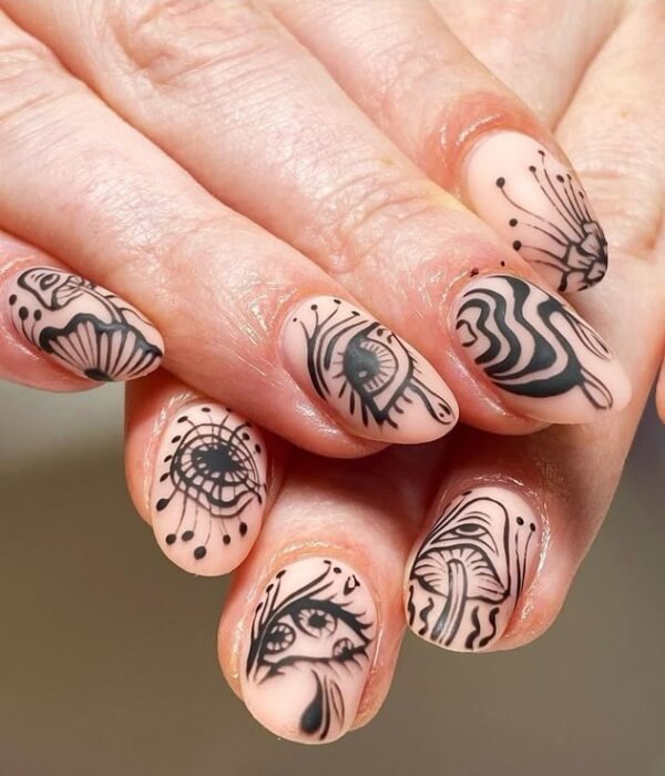 Close-up of nude nails featuring gothic symbol tattoo art with bold black abstract eyes, shells, and mystical linework designs.