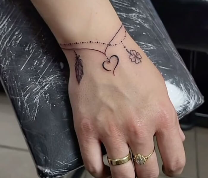 Mini Zodiac Armbands - Trending Tattoo Delicate mini zodiac armband tattoo with fine-line dots, heart symbol, feather, and floral accents around the wrist.