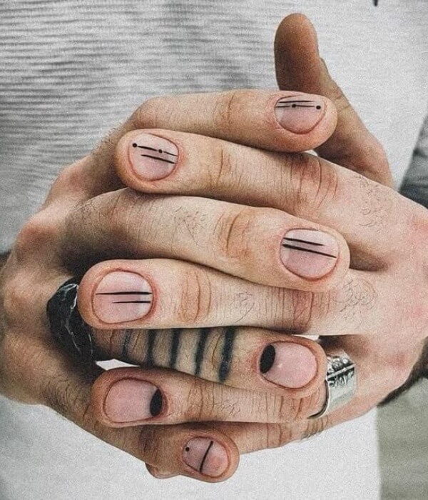 Close-up of clasped hands with short nude nails featuring minimalist black line nail tattoos, including dots, parallel lines, and simple geometric accents.