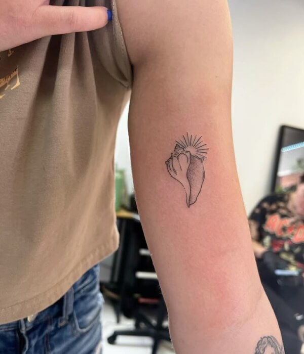 Minimalist shell tattoo on the inner arm featuring a simple line-art seashell with sun rays, creating a delicate and modern tattoo design.