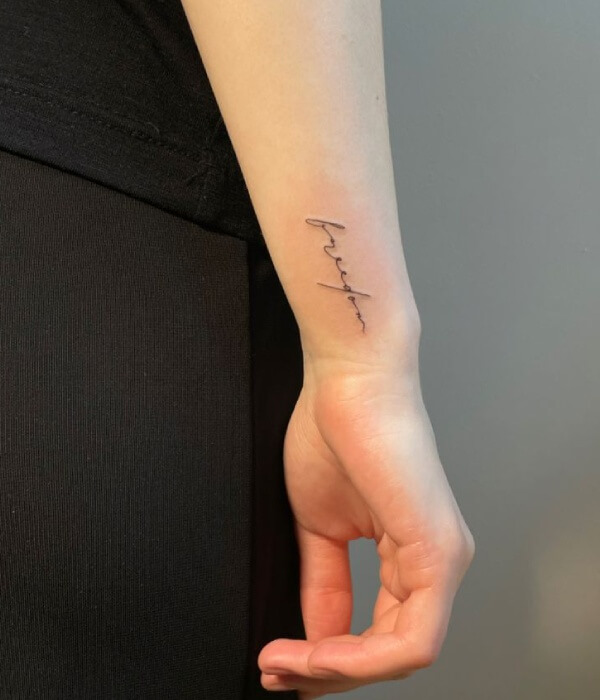 Minimalist fine-line name tattoo on a woman’s inner forearm, featuring the name “Andrea” in elegant cursive with a small heart and date beneath, in black ink.