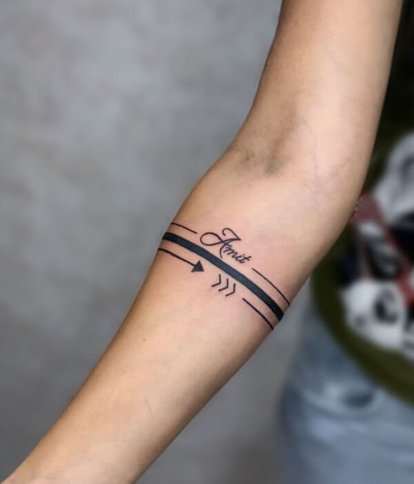 Geometric name tattoo on the inner arm featuring the name “Amit” in cursive, integrated with parallel line bands and arrow motifs in minimalist black ink.