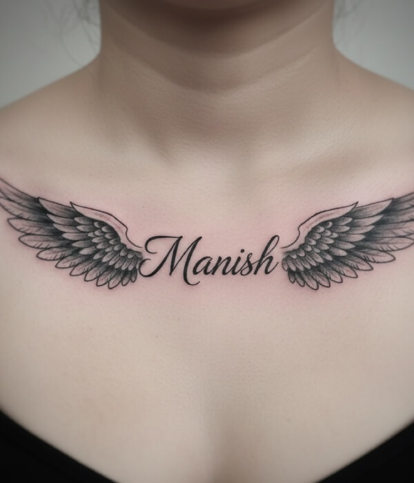 Name tattoo on a girl’s upper chest featuring the name “Manish” in elegant cursive, flanked by detailed symmetrical angel wings in black and grey shading, symbolizing protection and spirituality.