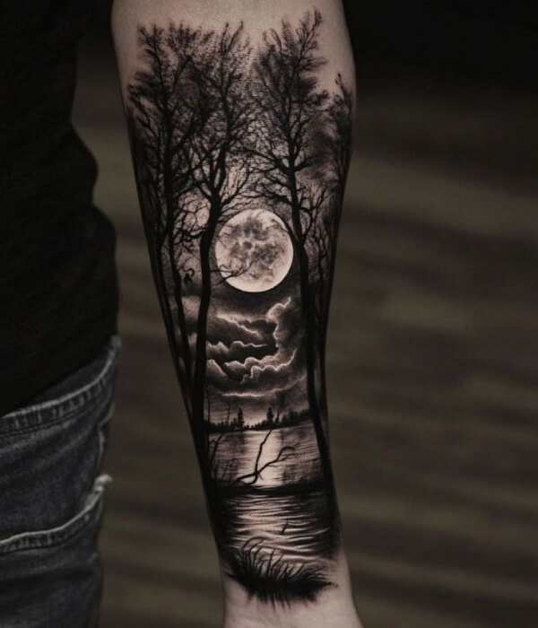 Dark night forest tattoo on a forearm, featuring silhouetted trees, a full moon, dramatic clouds, and reflective water in detailed black and grey realism style on real human skin.