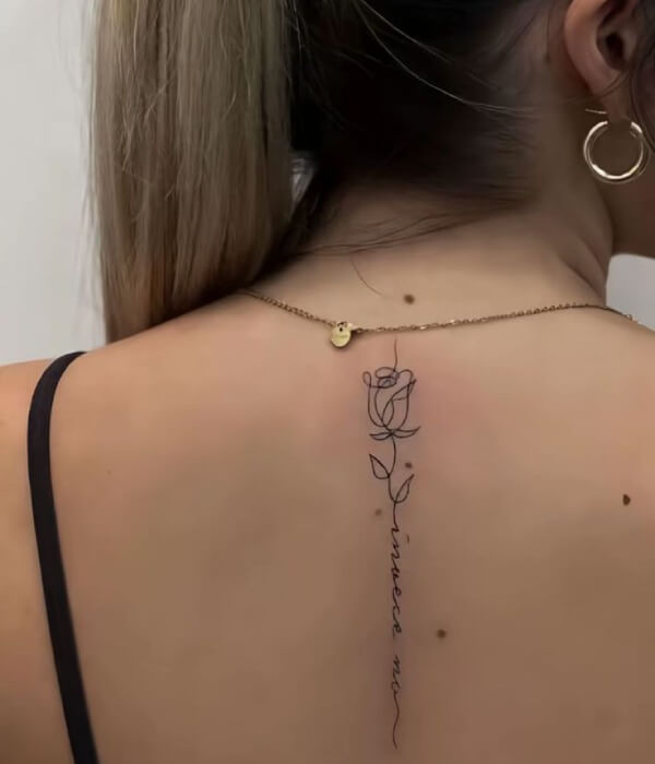 Minimalist spine name tattoo on a woman’s back, featuring a fine-line rose outline with a vertical cursive name running down the spine in delicate black ink.