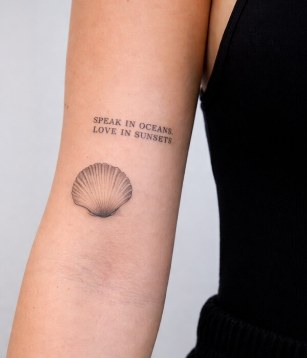 Minimalist seashell tattoo on the upper arm paired with the quote “Speak in oceans, love in sunsets,” featuring an elegant ocean-inspired tattoo design.