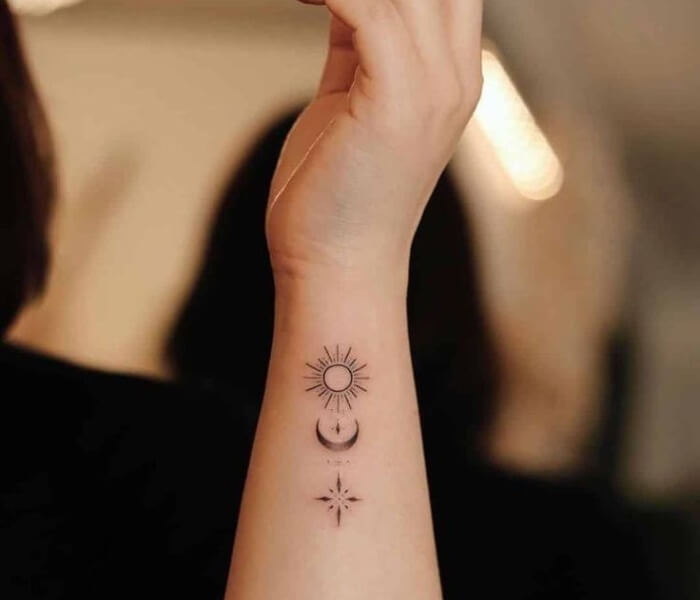 Tiny Moon Phases Tattoo on the Side of the Hand - Trending Tattoo Minimalist wrist tattoo featuring a sun symbol, crescent moon, and star in fine-line black ink.