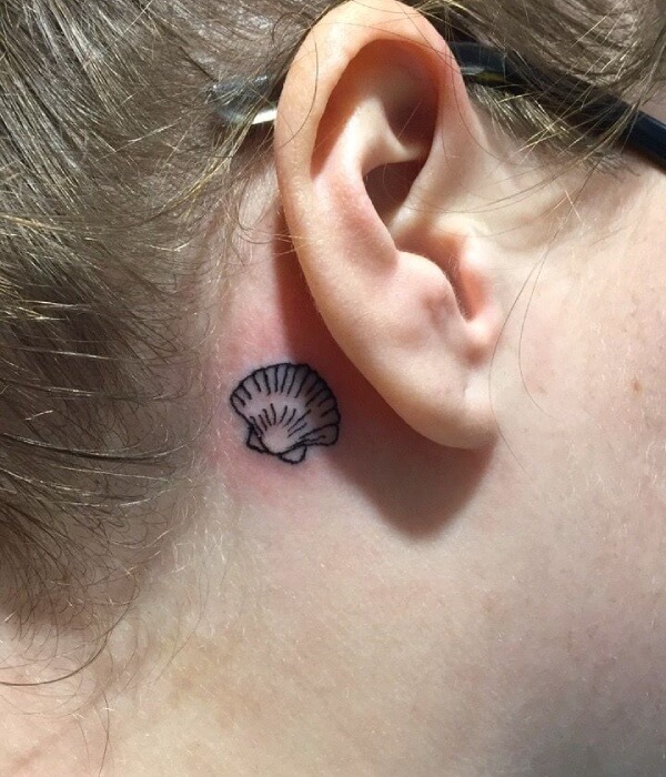 Tiny seashell tattoo behind the ear featuring a simple black line scallop shell design for a subtle and minimalist look.