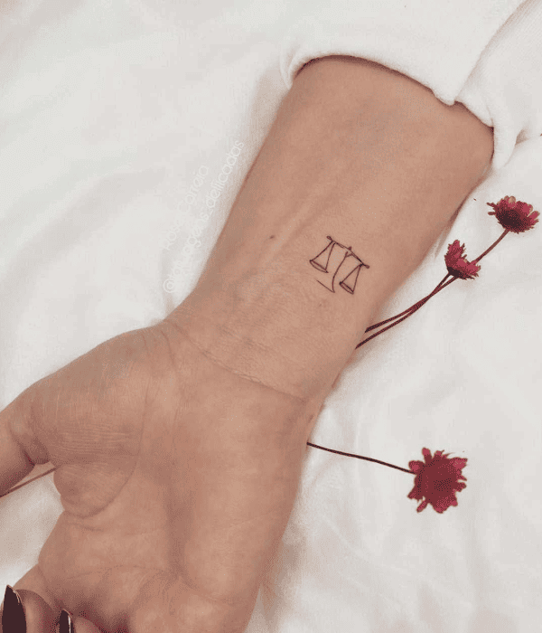 Minimalist Libra scales tattoo on the inner wrist, symbolizing balance, justice, and harmony.