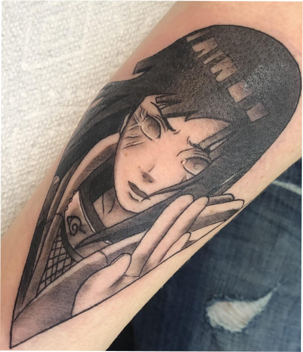 A striking black-and-grey tattoo of Hinata Hyuga from Naruto on an arm, capturing her in a combat stance with her Byakugan activated, featuring heavy blackwork hair and delicate shading.
