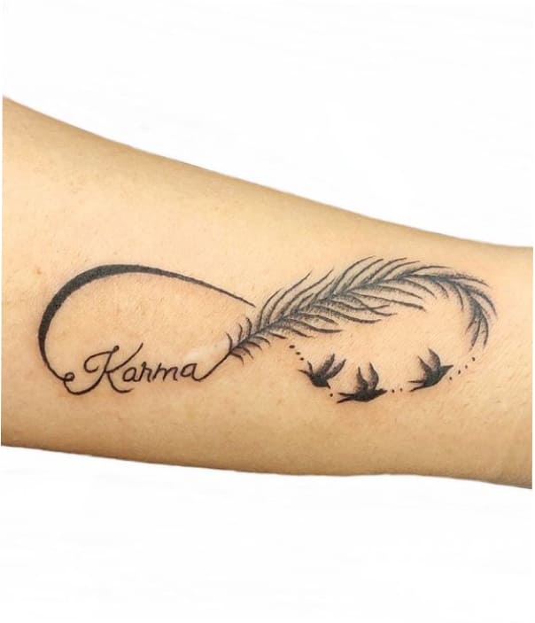 Alt text: Minimalist forearm tattoo featuring a flowing feather transforming into flying birds, with the word “Karma” written in elegant cursive script.