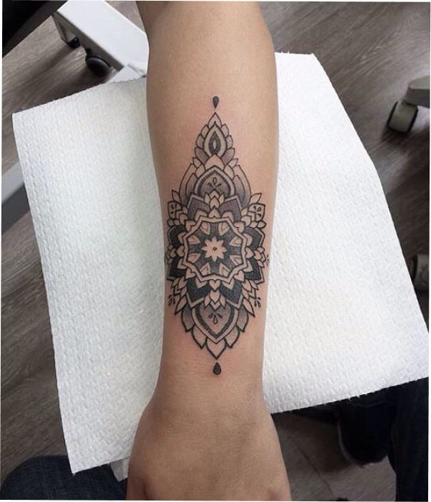 Black and grey mandala-style geometric tattoo centered on the inner forearm with symmetrical detailing.