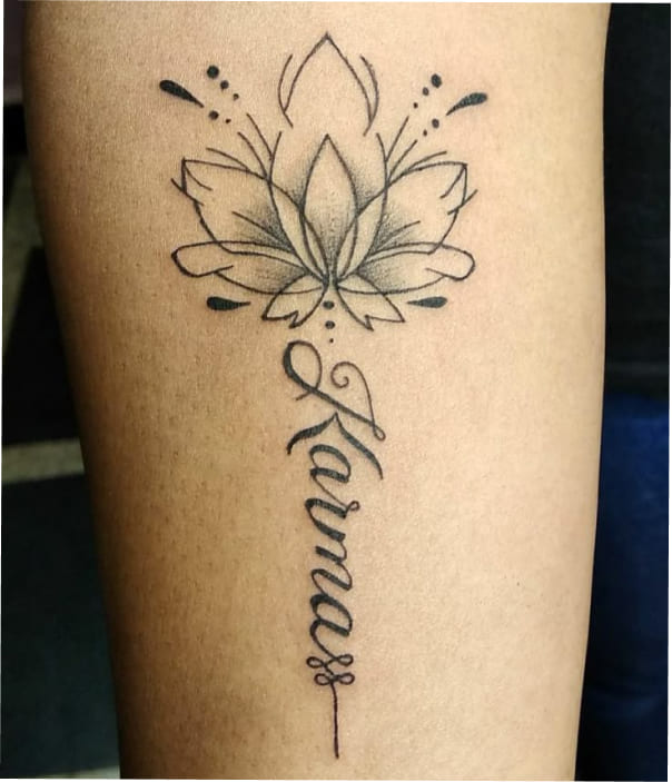 Elegant lotus flower tattoo with fine line detailing and the word “Namass” written vertically in flowing cursive script on the forearm.