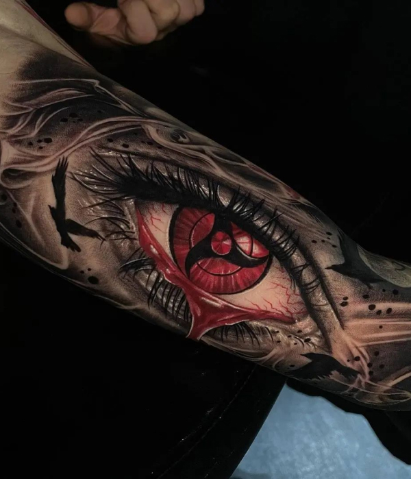 Hyper-realistic forearm tattoo of Itachi Uchiha's Mangekyou Sharingan eye from Naruto, featuring red irises and black crows on a dark background.