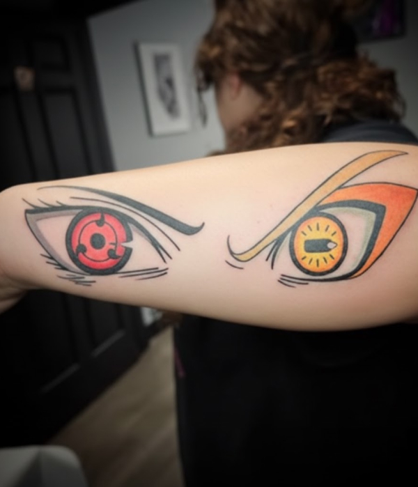 Vibrant anime tattoo on a forearm featuring a red Sharingan eye next to an orange Sage Mode eye, both with clean lines and saturated colors.