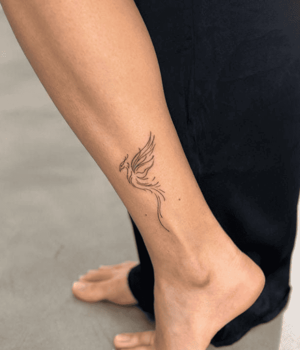 Minimalist phoenix outline tattoo on the inner ankle, symbolizing rebirth, strength, and new beginnings.