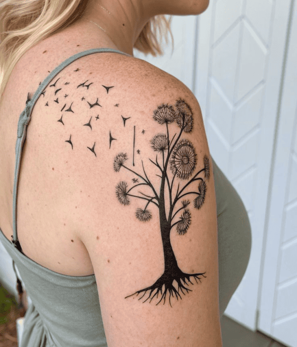 Black ink dandelion tree tattoo on the upper arm with birds in flight, symbolizing growth, freedom, and new beginnings.