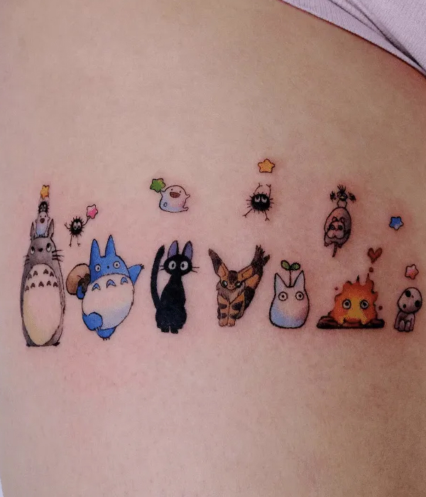 A horizontal row of small, colorful tattoos featuring various Studio Ghibli characters, including Totoro, Jiji the cat, Calcifer the fire demon, and a Kodama tree spirit, accented with tiny colorful stars.