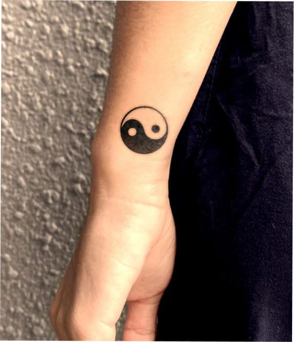 Small black yin-yang symbol tattoo on the inner wrist, representing balance and harmony.